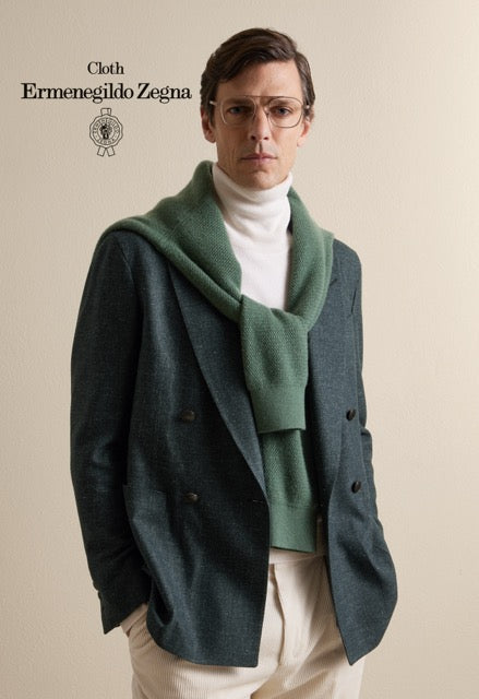 Model wearing a dark teal double-breasted jacket, a green sweater draped over the shoulders and cream trousers; Ermenegildo Zegna cloth reference 67030.
