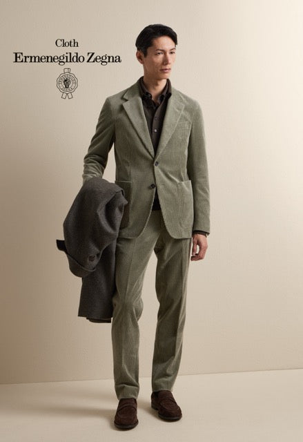 Model wearing an olive green single-breasted suit and brown shirt, carrying a jacket; Ermenegildo Zegna cloth reference 67052.