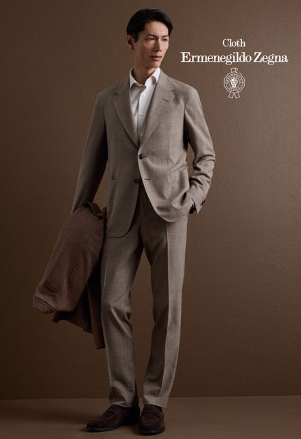 Model wearing a taupe single-breasted suit and white shirt, carrying a brown jacket; Ermenegildo Zegna cloth reference 67060.
