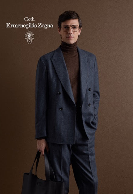 Model wearing a blue double-breasted suit and brown turtleneck, carrying a black bag; Ermenegildo Zegna cloth reference 67070.