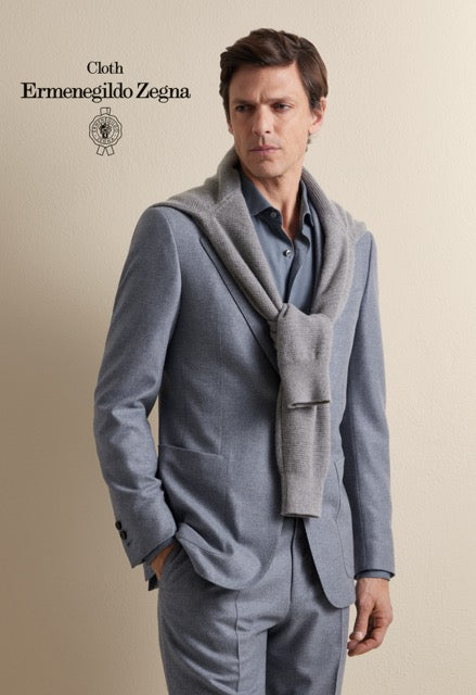 Model wearing a light blue suit and shirt with a grey sweater draped over the shoulders; Ermenegildo Zegna cloth reference 67072.