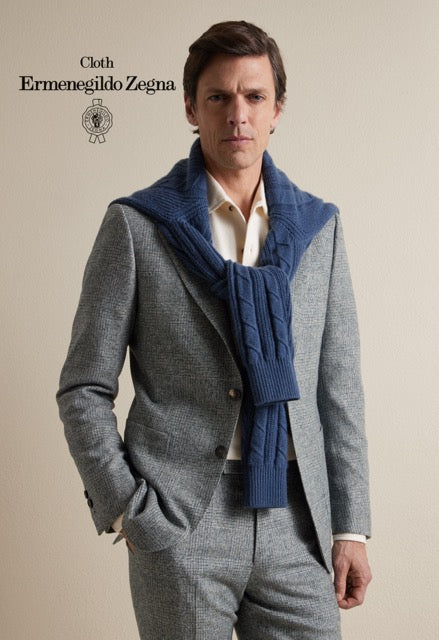 Model wearing a grey patterned suit and cream shirt with a navy cable-knit sweater draped over the shoulders; Ermenegildo Zegna cloth reference 67077.