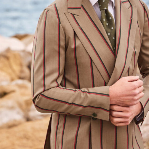 Close-up of a tan double-breasted suit crafted from Ariston Italian fabric, featuring bold navy and burgundy vertical stripes, peak lapels, and refined Mediterranean-inspired tailoring.