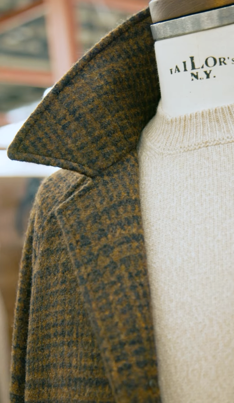 Close-up of an olive and brown checked coat with a raised collar over a cream knit sweater.