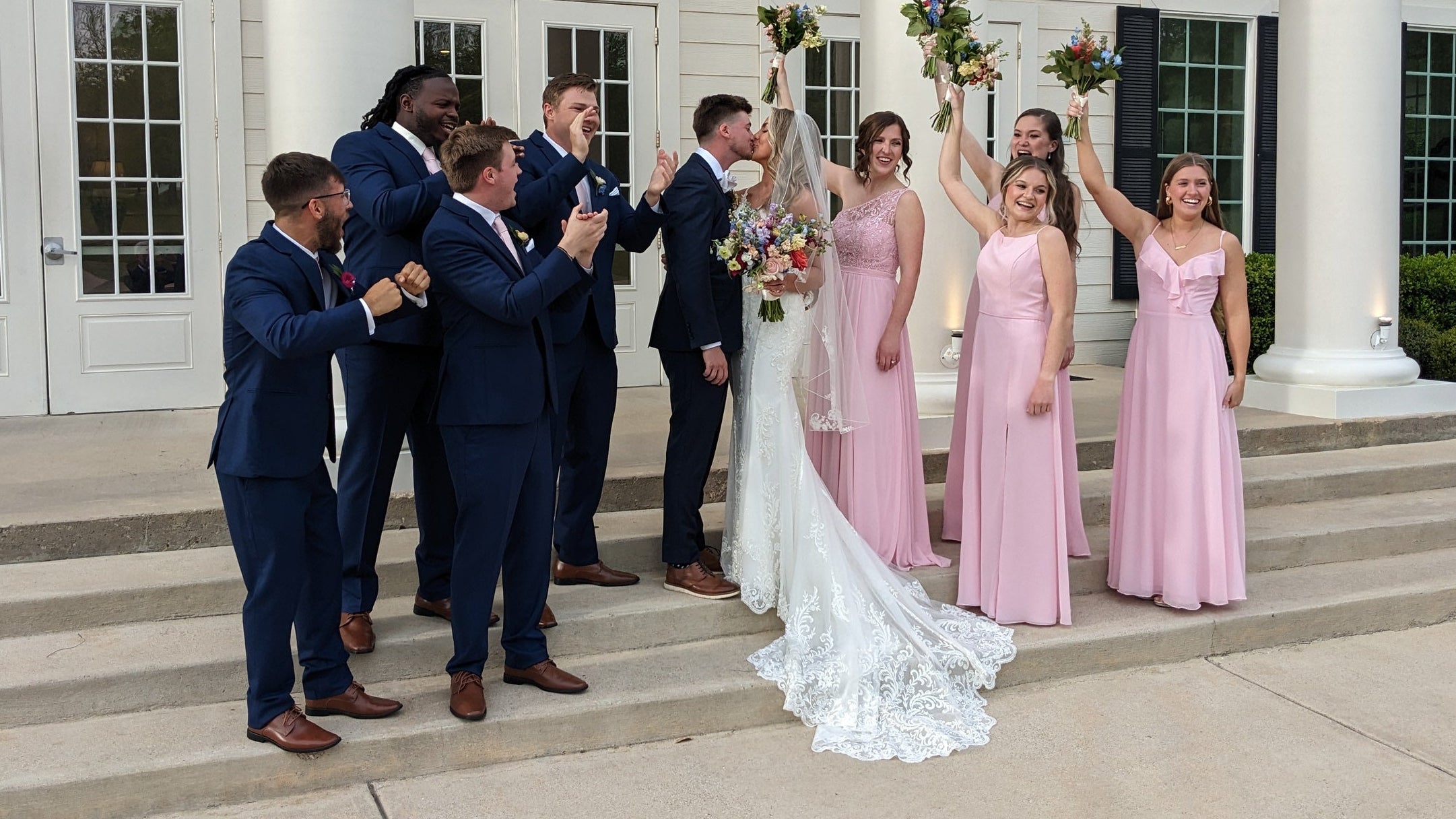 Bride and groom celebrating with their wedding party, featuring custom navy suits by Jeffrey Bartlett Clothiers for the groom and groomsmen.