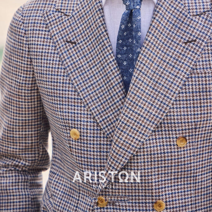 Close-up of a blue and tan houndstooth double-breasted jacket crafted from Ariston Italian fabric, showcasing refined tailoring, peak lapels, and a textured blue tie.