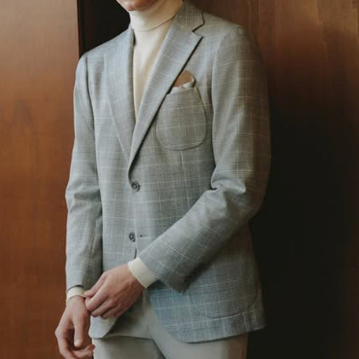 Light gray windowpane sport coat crafted from Dormeuil luxury fabric, styled with a cream turtleneck and pocket square for refined contemporary tailoring.