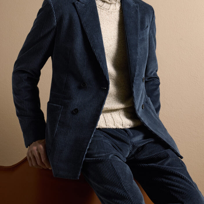 Man wearing a navy corduroy suit crafted from Ermenegildo Zegna Italian fabric with a cream knit sweater, showcasing refined casual tailoring.