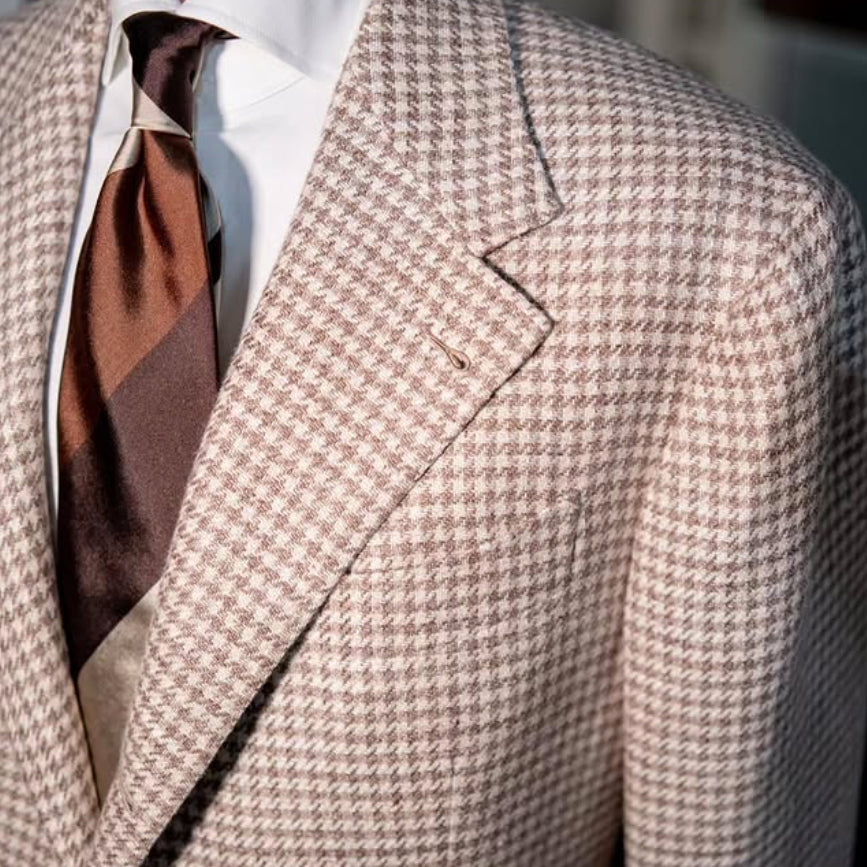 Close-up of a cream houndstooth sport coat crafted from Lanificio Cerruti Italian fabric, showcasing the refined weave, notch lapel, and rich brown silk tie.